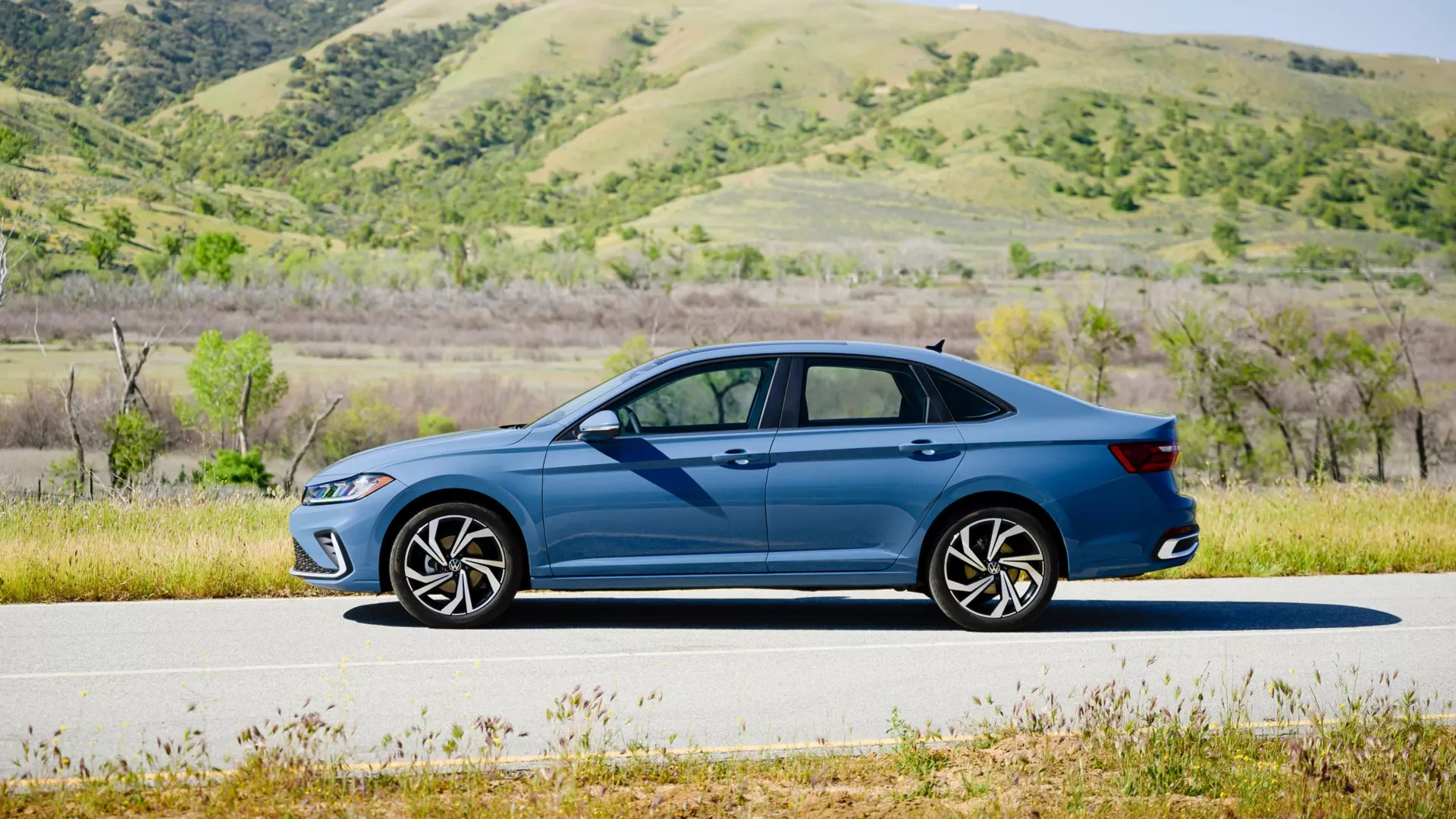 2026 Volkswagen Jetta side profile in blue on a two lane road, the compact sedan sold in Jacksonville NC