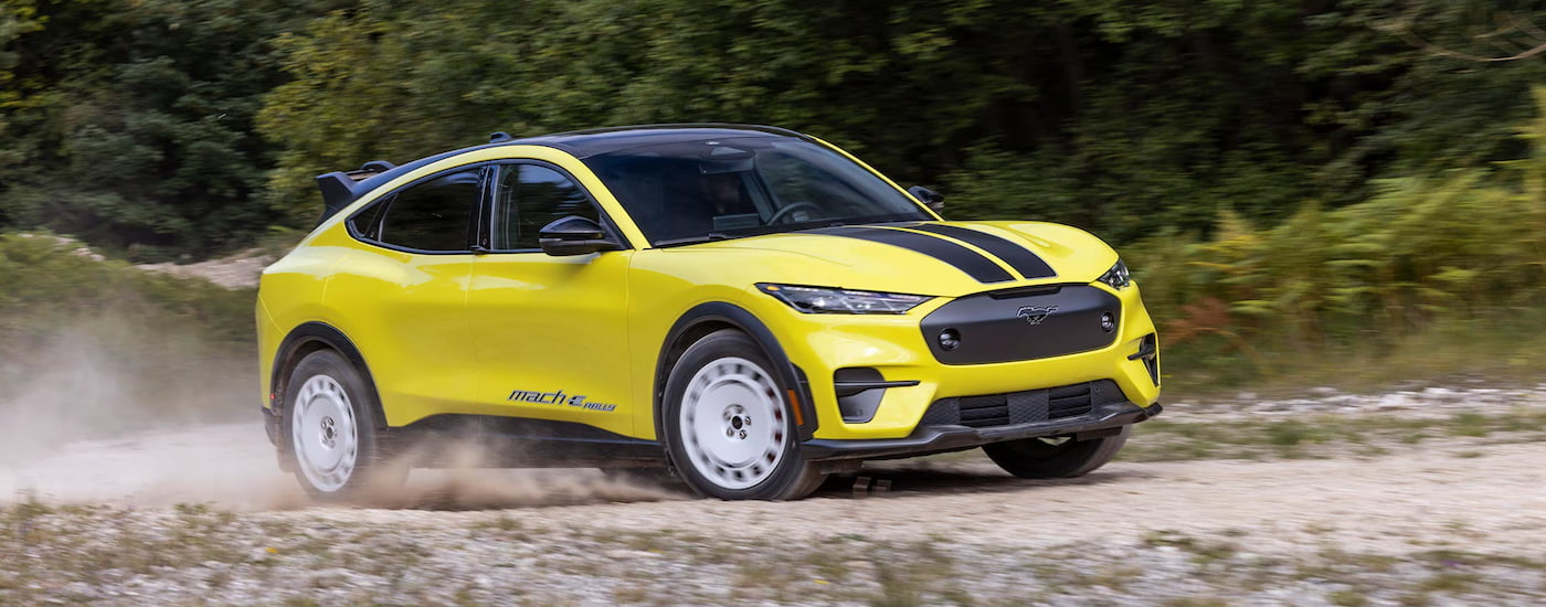 A yellow 2024 Ford Mustang Mach-E Rally Edition driving on a dusty track.