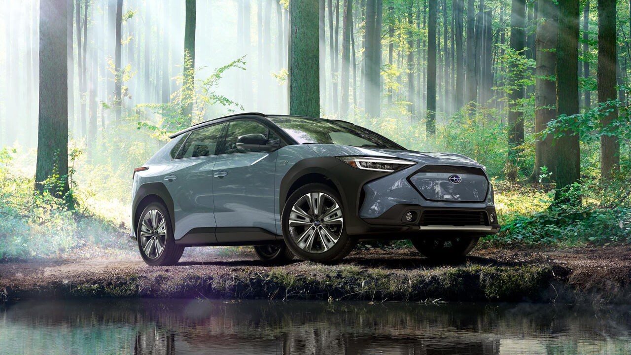 vue latérale avant d'une Subaru Solterra 2023 près d'un plan d'eau en forêt