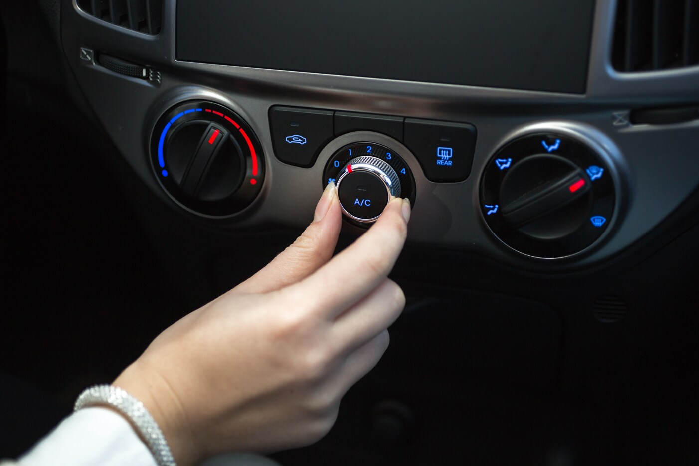 A person's right hand turning the air conditioning knob in a vehicle A person's right hand turning the air conditioning knob in a vehicle