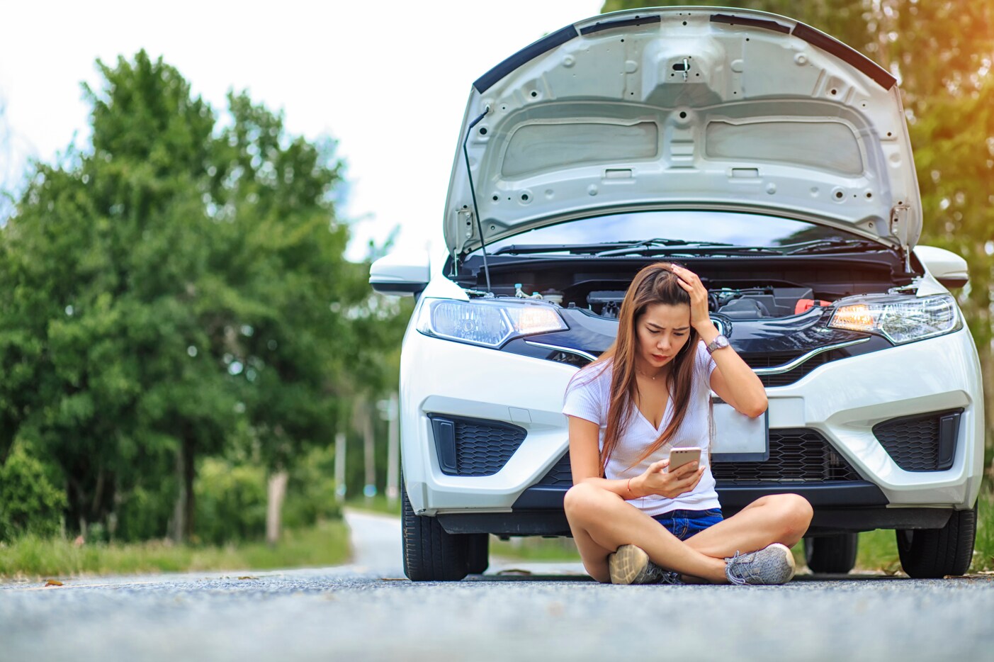 A frustrated driver sitting in front of a broken-down car on the side of the road A frustrated driver sitting in front of a broken-down car on the side of the road