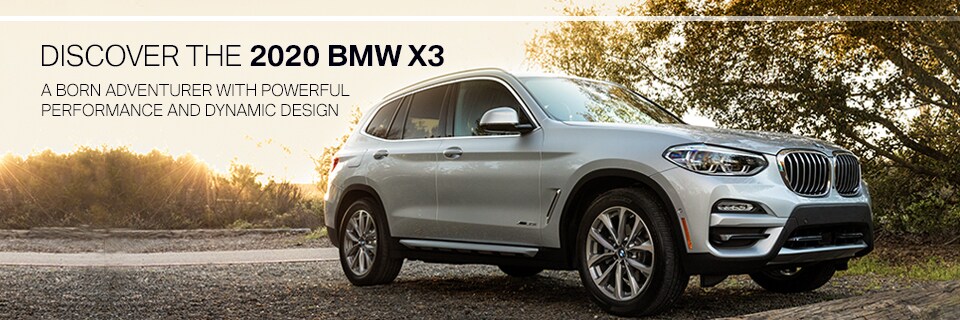 Discover the 2020 BMW X3 - Born Adventurer with Powerful performance and dynamic design. Silver BMW X3 M parked in gravel lot by treesh and field