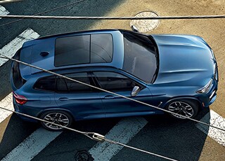 Birdseye vie of blue BMW X3 driving across crosswalk