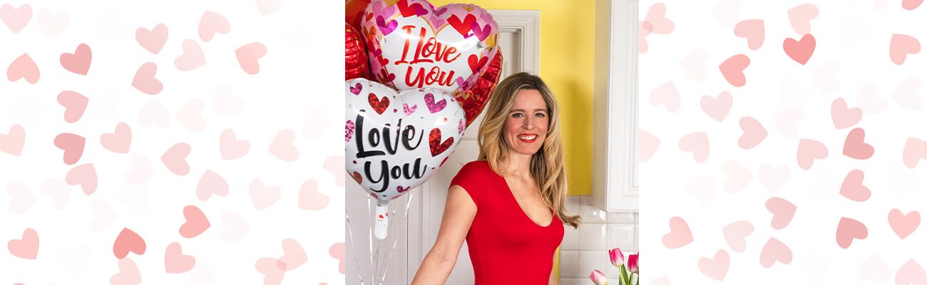 Aurora holding heart balloons in front of a pink background with hearts on it
