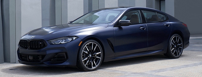 Dark blue BMW 8 Series Gran Coupe parked in front of a sleek concrete building with vertical columns