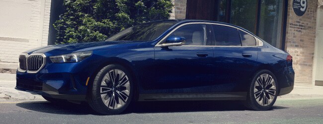 Side view of a blue BMW 5 Series parked on a city street near modern brick and glass buildings