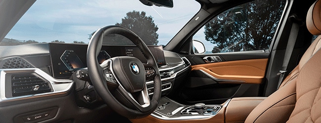 Premium BMW X5 SUV interior with brown leather seating, panoramic digital display, and natural light