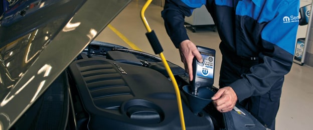 A MOPAR service technician pouring oil into a vehicle A MOPAR service technician pouring oil into a vehicle