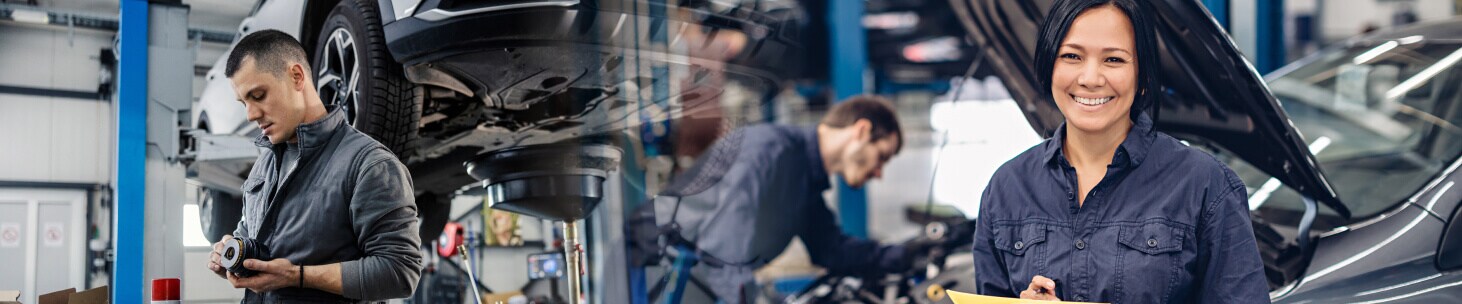 Auto mechanics inspect auto parts and smile while holding a clipboard.