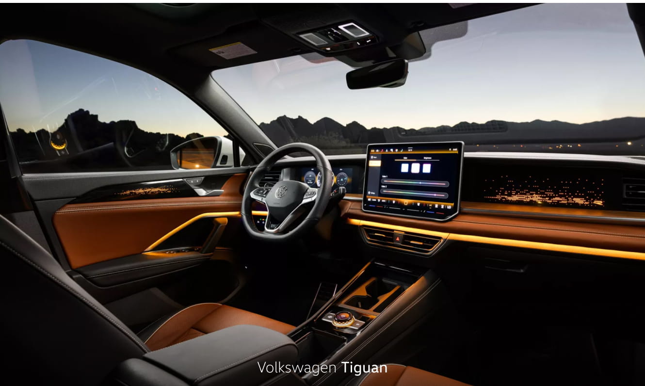 Volkswagen Tiguan interior featuring a digital driver display, large touchscreen infotainment system, and ambient lighting with a mountain sunset visible through the windows.