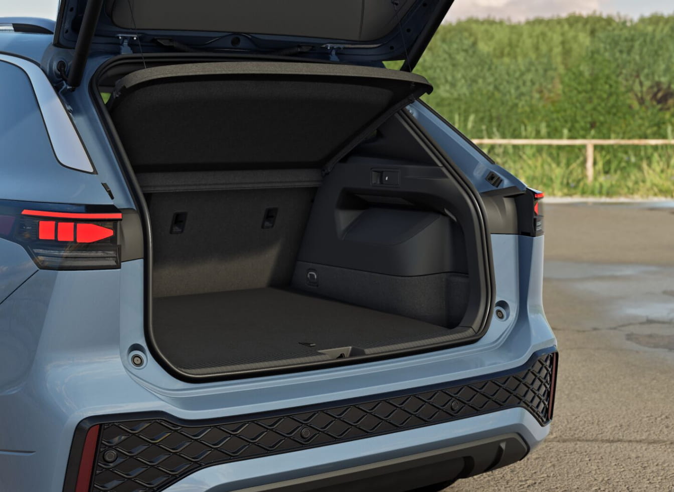 Open trunk of a light blue Volkswagen Tiguan SUV showing spacious, empty cargo area. Tail lights are illuminated. Background features greenery and pavement.