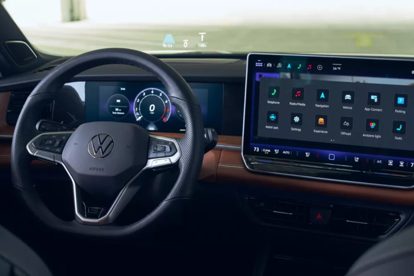 Volkswagen Tiguan showing a sleek steering wheel, digital dashboard, and a large infotainment screen displaying app icons. The ambiance is high-tech and clean.