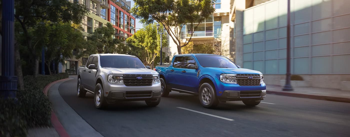 2022 Ford Maverick - Duo.jpg .A silver and a blue 2022 Ford Maverick are shown driving down a city street next to each other.