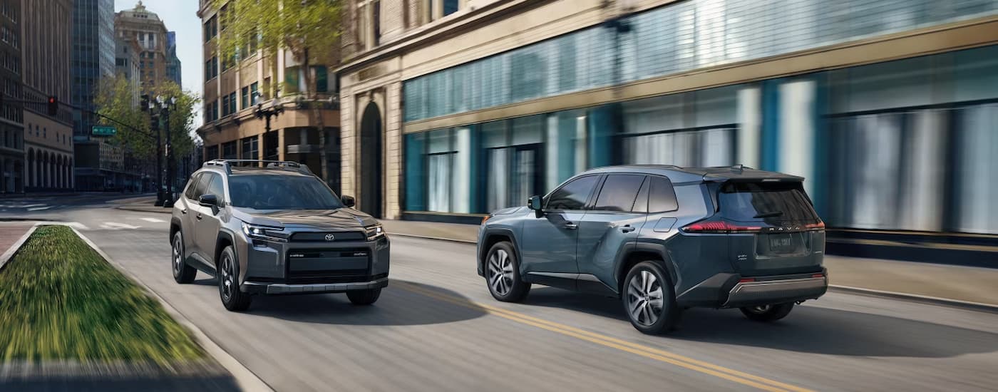 2026%20Toyota%20RAV4.jpg A blue and a grey 2026 Toyota RAV4 driving on a city street