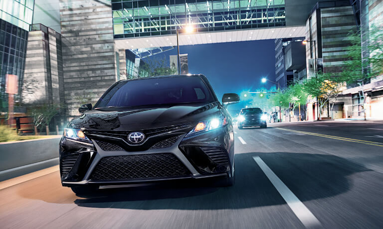 2020 Toyota Camry in black driving at night head on in a city