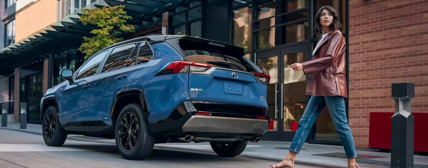 Toyota RAV4 Hybrid for Sale - 2023 Toyota RAV4 XSE Hybrid - Blue Walking.jpg A woman is shown walking behind of a blue 2023 Toyota RAV4 XSE Hybrid parked on the side of a street.