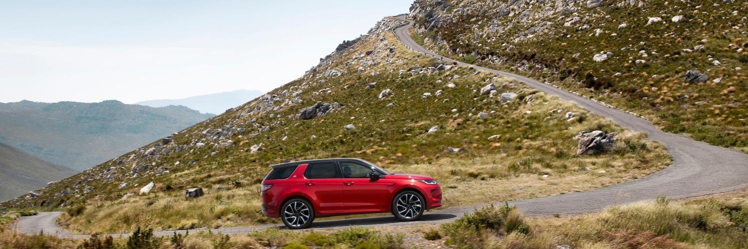 2024 Discovery Sport SUV Red 2024 Discovery Sport SUV driving down curved mountain road
