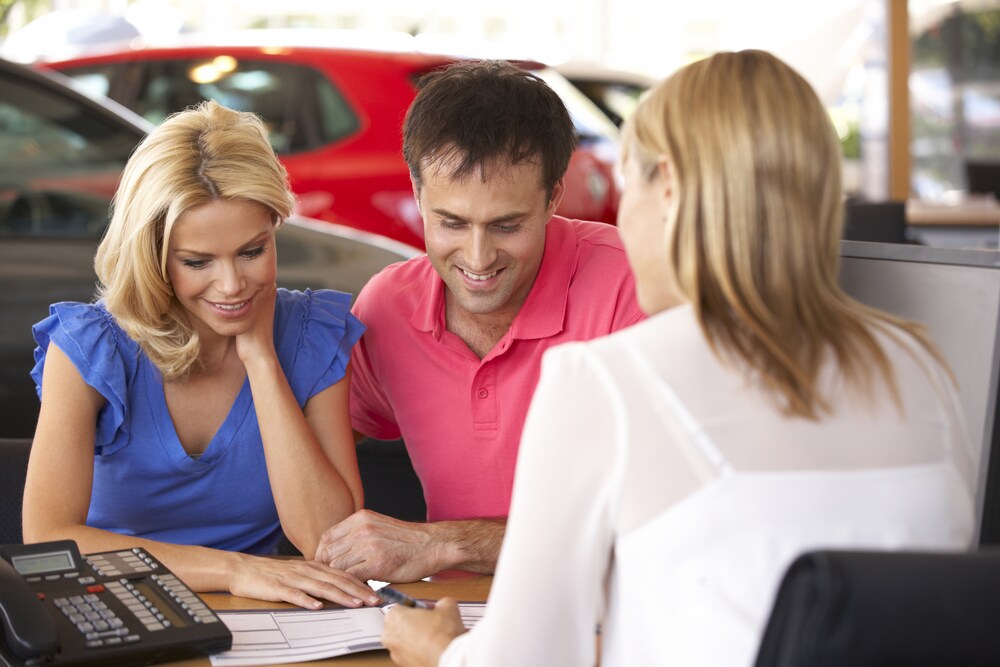 Two people meeting with an auto dealership team member at a desk Two people meeting with an auto dealership team member at a desk