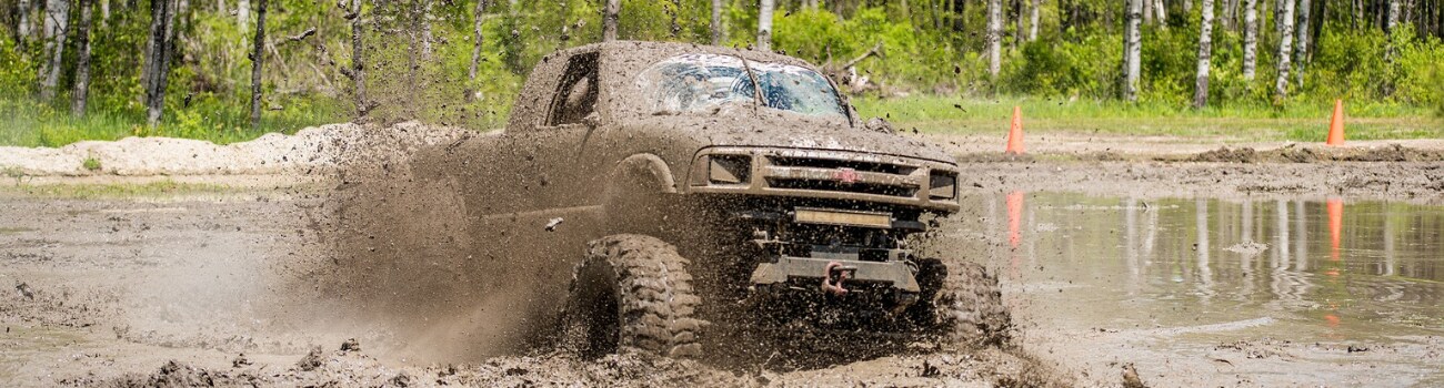 Best used 4x4 trucks in Colorado Springs Phil Long Valucar.png A used 4x4 Chevy truck plowing through deep mud with mud covering the entire truck