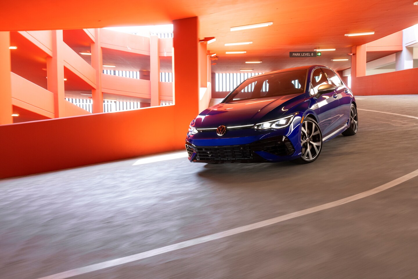 blue Volkswagen Golf R driving down an orange painted parking structure