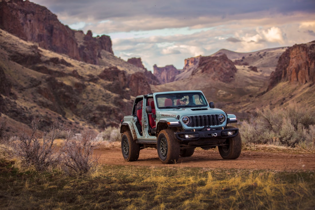 light green Jeep Wrangler SUV parked in the desert with the roof and doors removed
