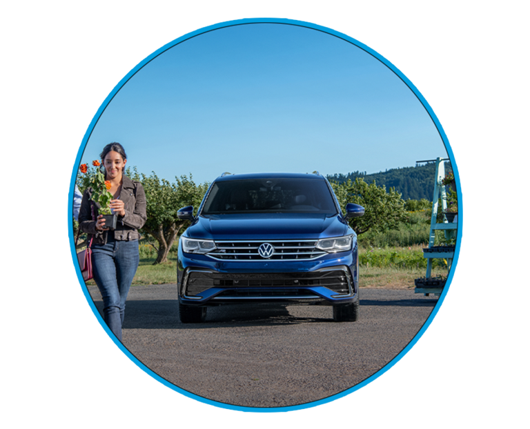 Woman walking with a flower in front of an Atlantic Blue Metallic Volkswagen Tiguan