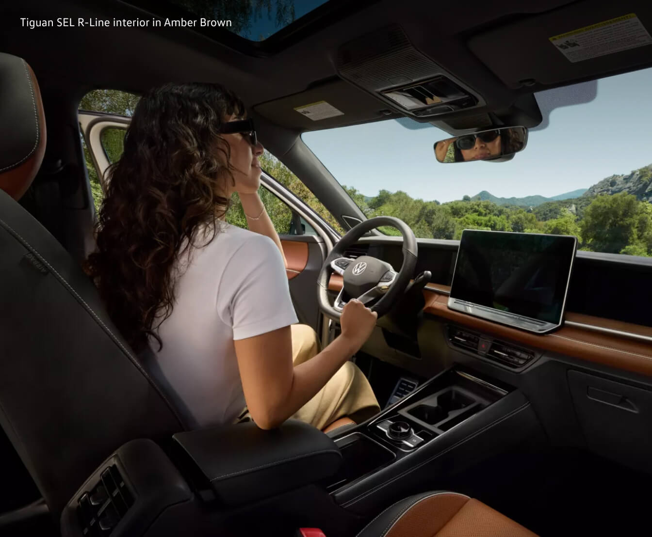 Over-the-shoulder view of a woman behind the wheel of a Volkswagen Tiguan SEL R-Line showcasing the dashboard.