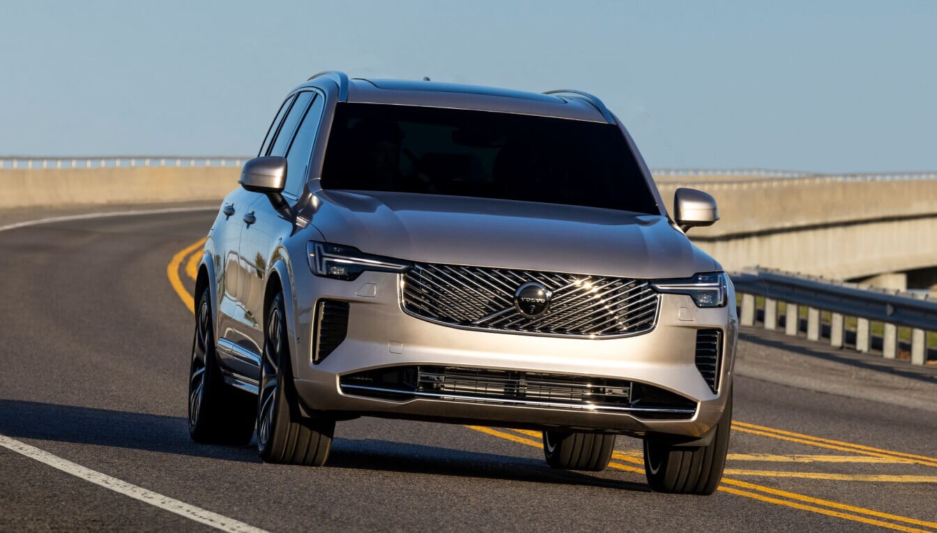 A silver 2026 Volvo XC90 parked in a seaside parking lot at golden hour.