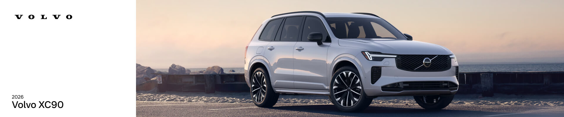 A silver 2026 Volvo XC90 parked in a seaside parking lot at golden hour.