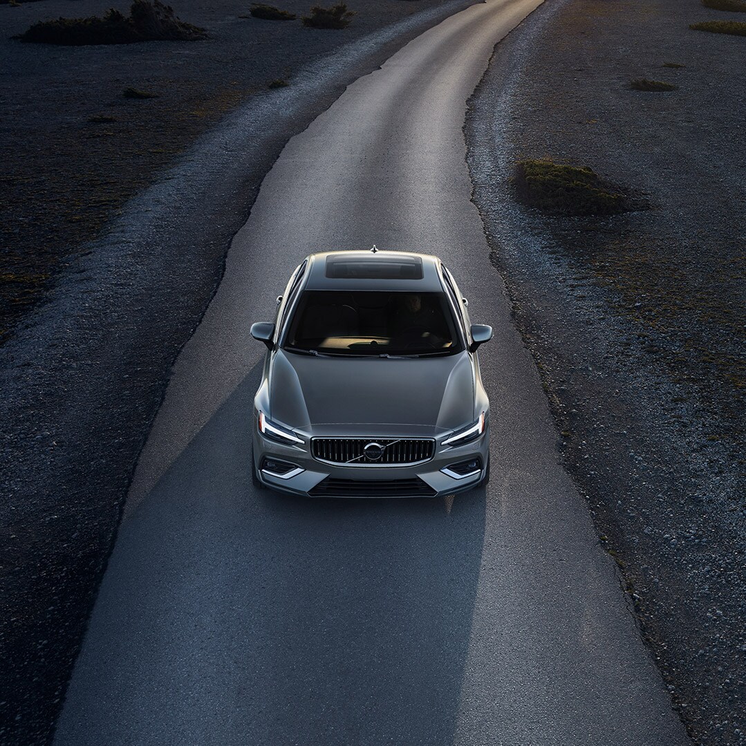 Volvo Cars New Bern is a Volvo Dealership in New Bern near Morehead City NC | Silver MY20 Volvo S60 driving down empty road at dusk