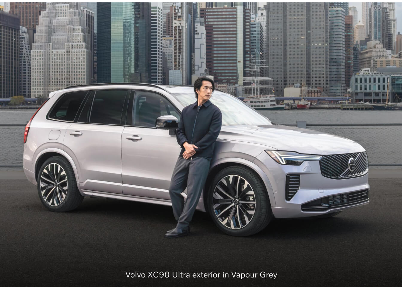 Volvo XC90 Ultra with a man leaning on the front fender against a city skyline.
