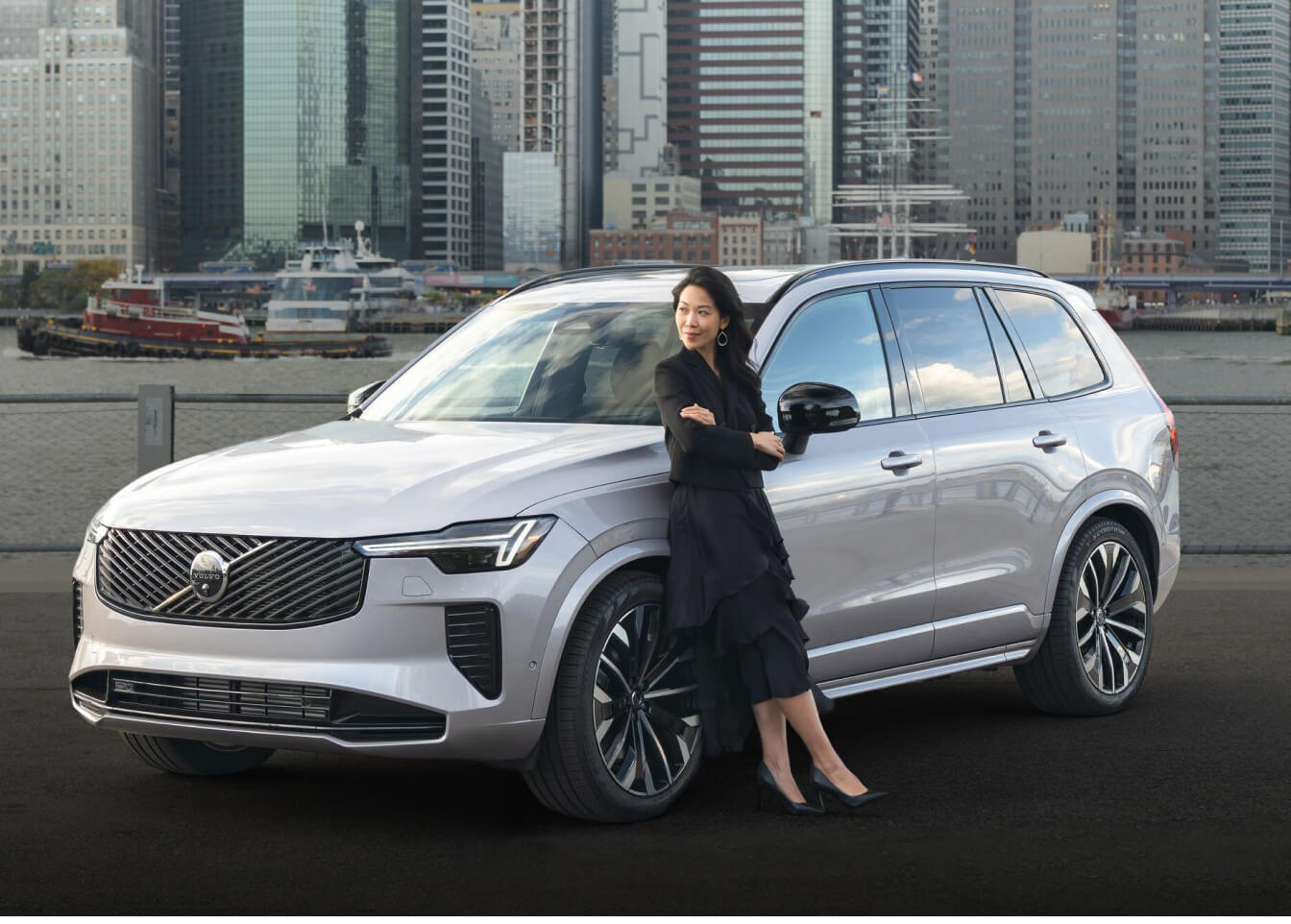 Volvo XC90 Ultra parked with a woman leaning on the fender by a city harbor.