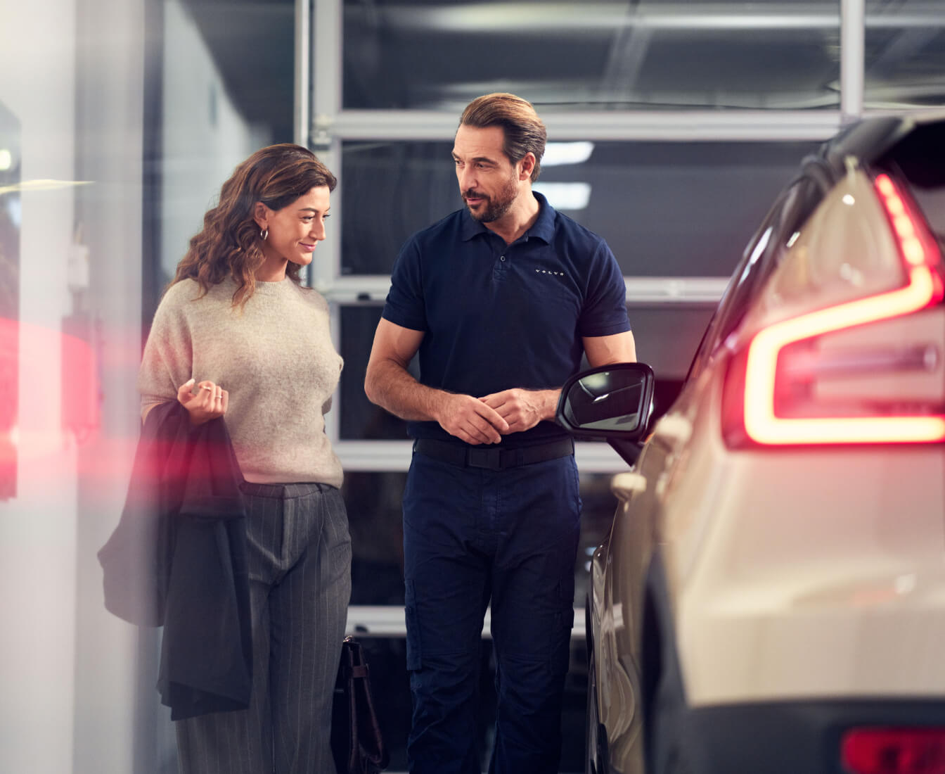 Volvo Cars staff member explains vehicle models to a customer beside a Volvo in the dealership.