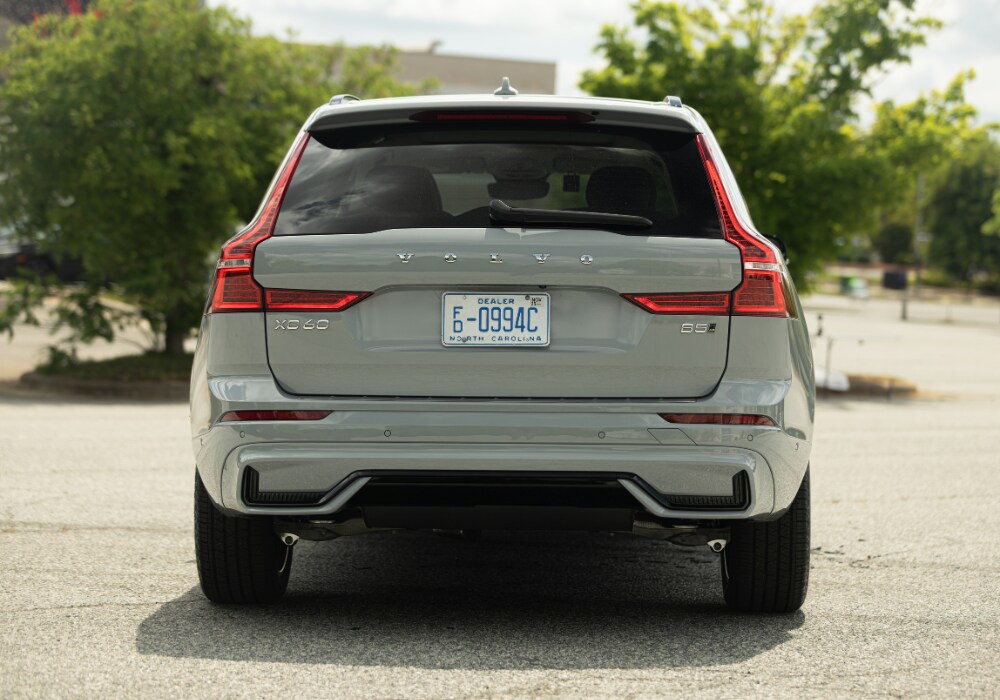 volvo-xc60-for-sale-burlington-nc.png Rear exterior view of the 2025 Volvo XC60 parked in a lot. The car is light gray and there are trees in the background