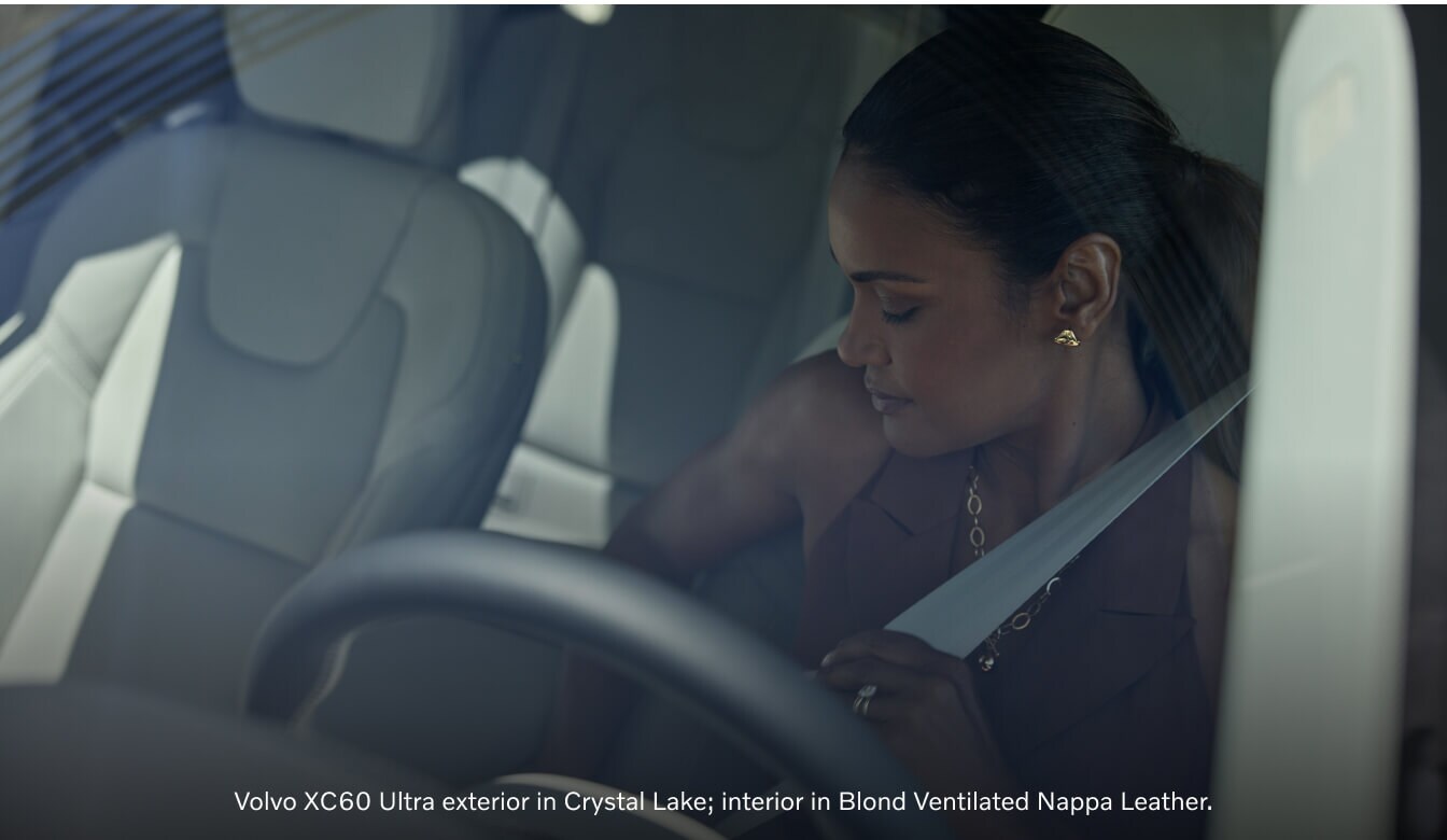 Interior profile view of a 2026 Volvo XC60 Ultra showing a female passenger fastening her seatbelt.