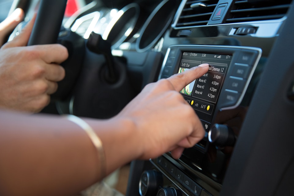 Woman's hand on Volvo display in car with drivers hands on steering wheel in background.jpeg