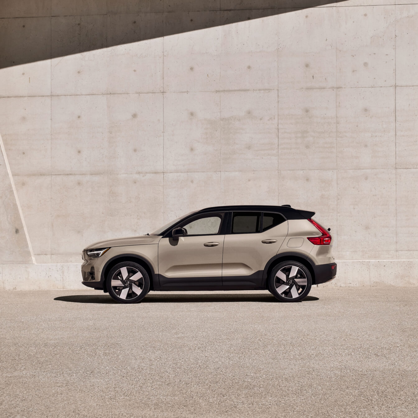 Side profile view of beige Volvo EX40 with black roof against a concrete wall background.