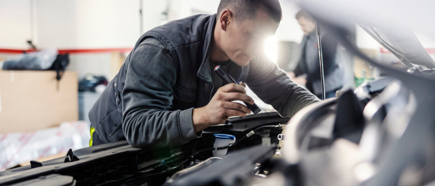 Service technician inspecting under hood with flashlight