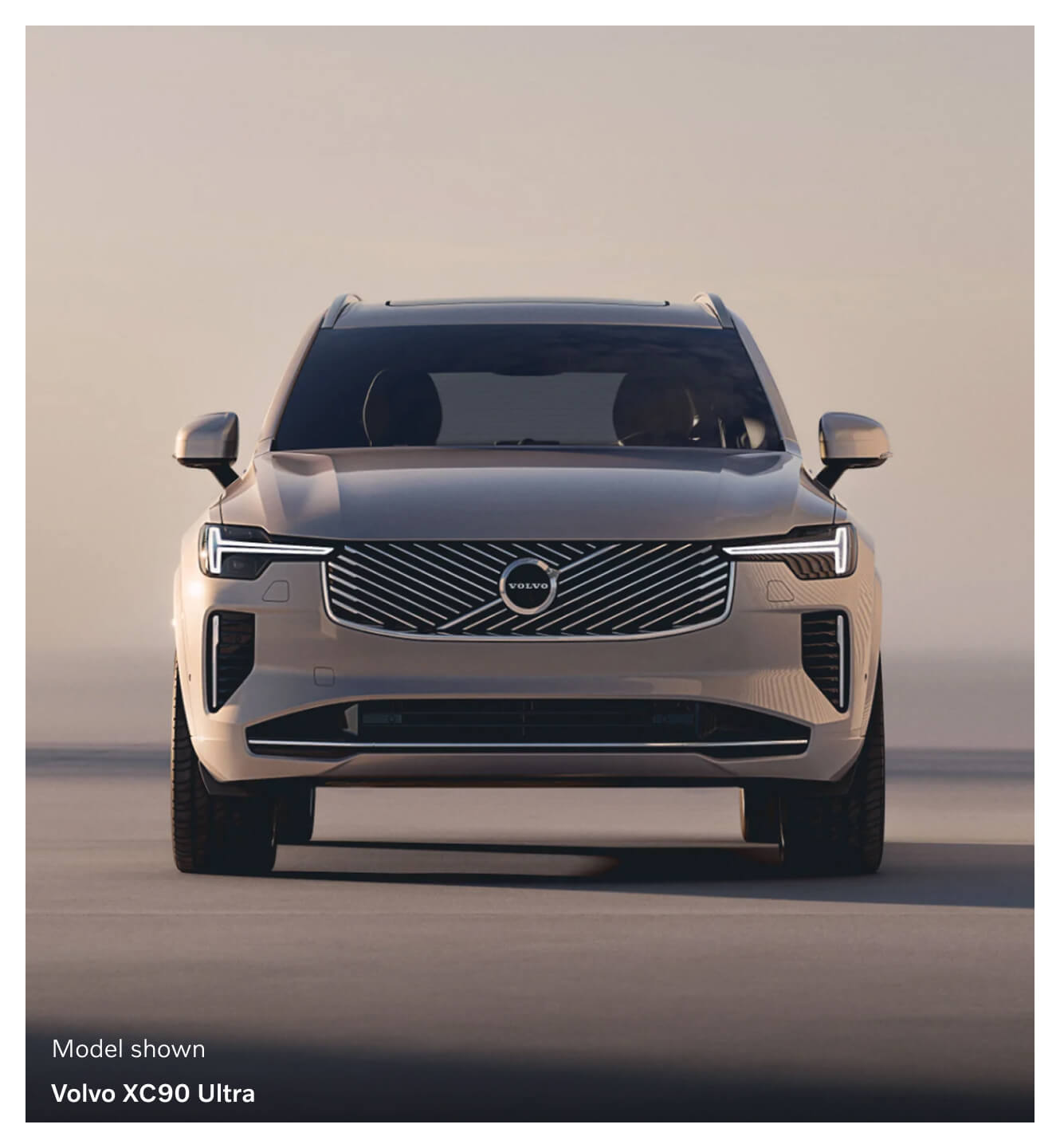 A front view of a beige Volvo XC90 Ultra parked on a minimal outdoor backdrop at golden hour.
