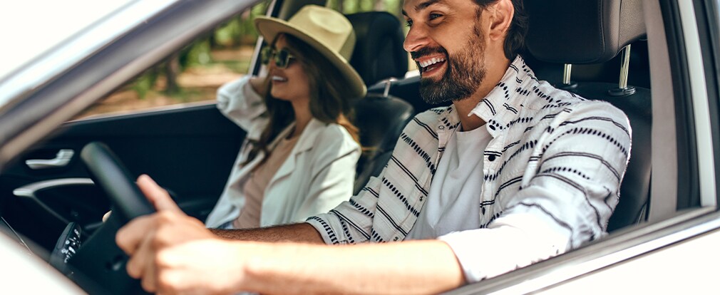 Learn Maintenance Warning Signs at West Broad Hyundai in Henrico, VA | Man driving his car during the day while smiling and a woman in the passenger seat smiling as well