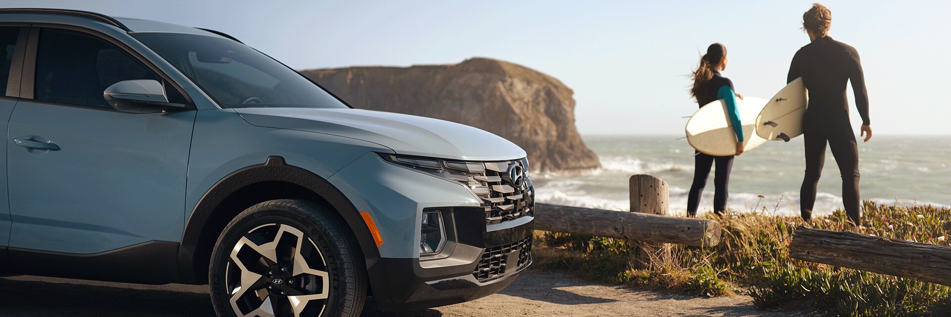 Basic Car Maintenance and Servicing Checklist | West Broad Hyundai | Two People with Surfboards Standing by Water with 2022 Hyundai Santa Cruz Parked Half Way in Frame on Left