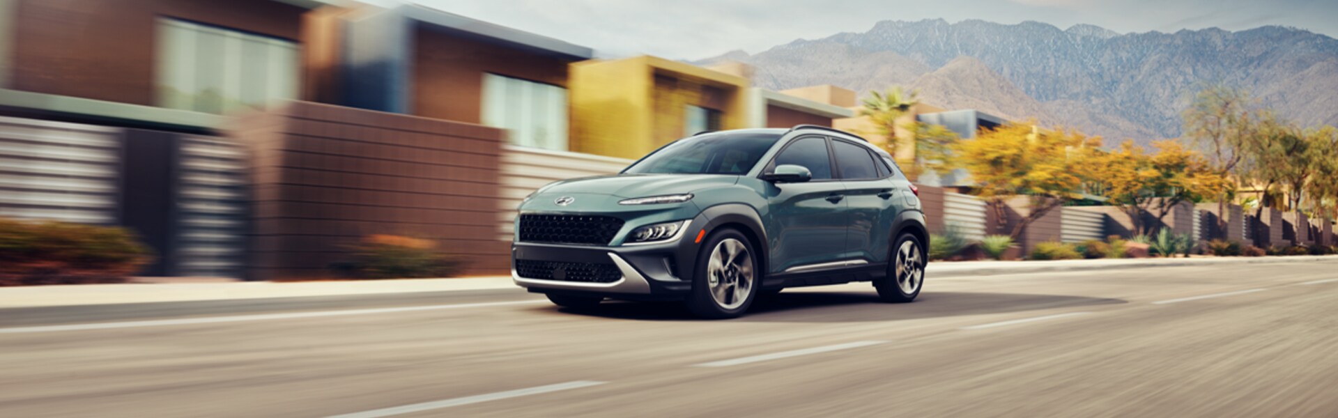 Performance features of the 2022 KONA Electric at West Broad Hyundai of Henrico | Gray-green 2022 Hyundai Kona driving down a suburban road with motion blur