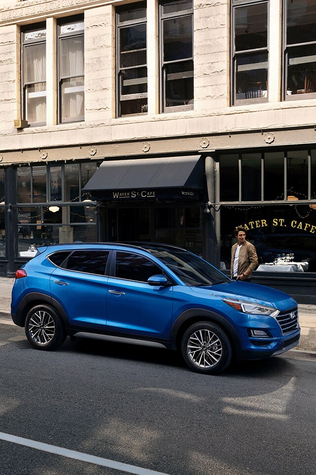 Things to Check When Buying a Used Car | West Broad Hyundai in Henrico, VA | Man Walking Towards Blue 2021 Hyundai Tucson Ultimate Facing Right Parked in Front of Cafe