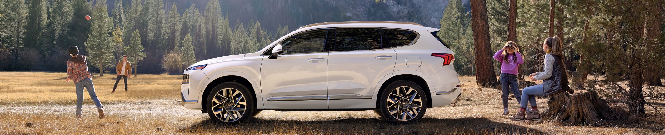 2023 Hyundai Santa Fe at West Broad Hyundai | Side view of a white 2023 Santa Fe parked in the woods with family members around it