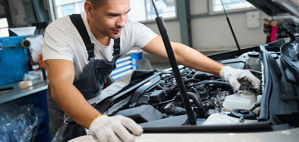 Learn Maintenance Warning Signs at West Broad Hyundai in Henrico, VA | Mechanic in white and black uniform is checking the coolant level of car engine under the hood