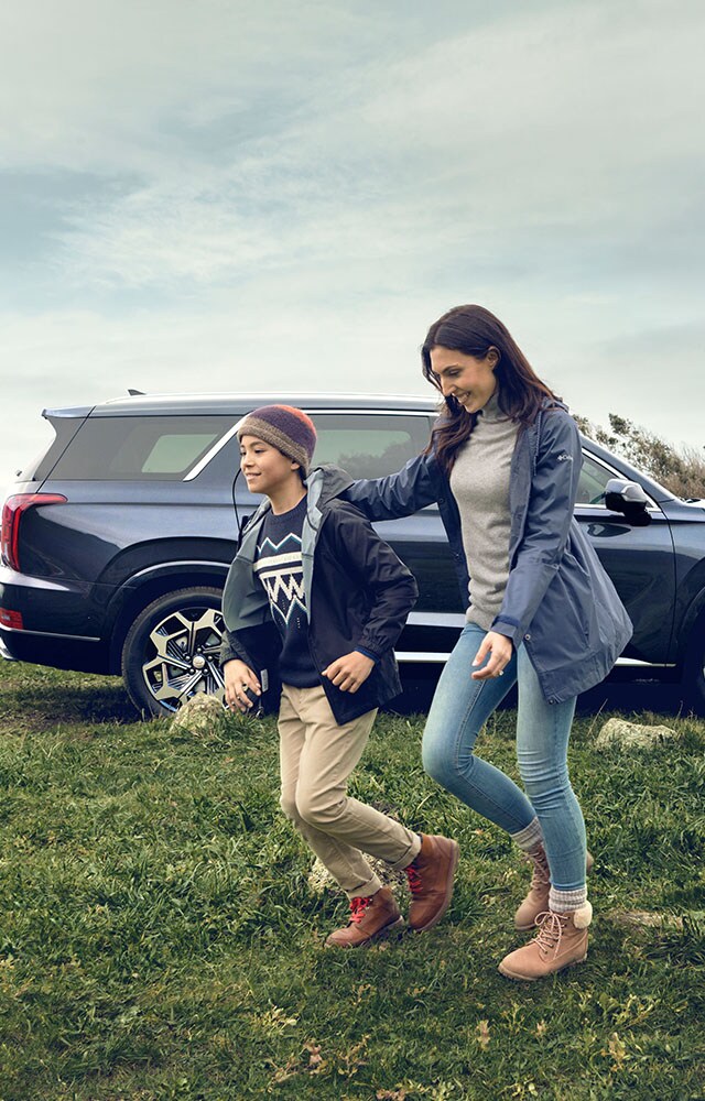 Accessories that help keep your Hyundai protected at West Broad Hyundai in Henrico, VA | Mother and Son Running in Front of Parked Hyundai Palisade Calligraphy