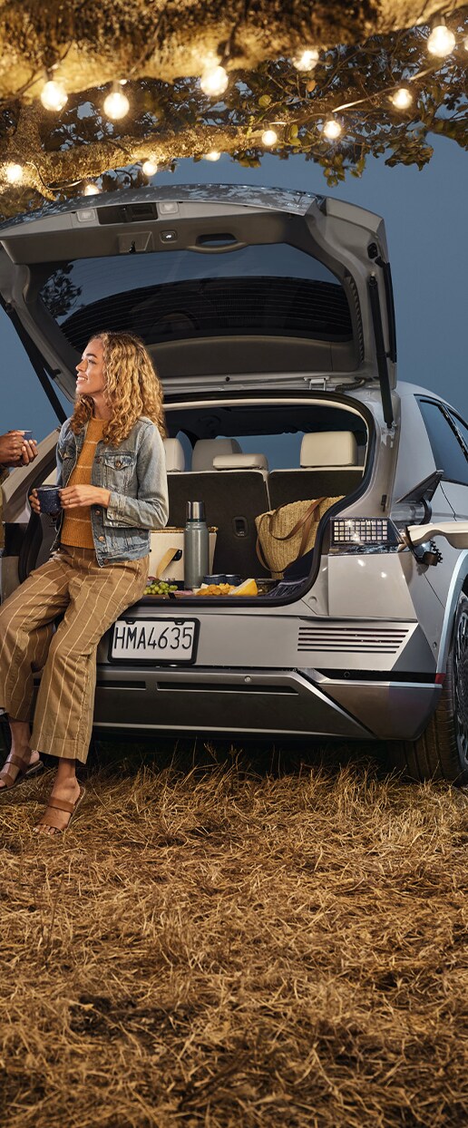 Accessories that help keep your Hyundai protected at West Broad Hyundai in Henrico, VA | Woman sitting on the edge of the trunk of her 2023 Hyundai Ionic 5 at night