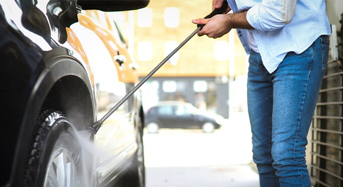 How to Get Your Car Summer Ready at West Broad Hyundai in Henrico, VA | Person in baby blue shirt and jeans washing black car using a water pressure hose