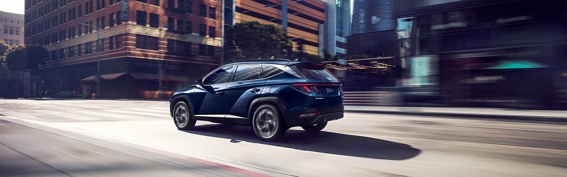 Performance features of the 2022 Tucson Hybrid at West Broad Hyundai of Henrico | Blue 2022 Hyundai Tucson driving down a city road with motion blur