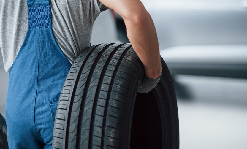 Extend the Life of Your Vehicle at West Broad Hyundai in Henrico, VA | Mechanic wearing blue uniform and grey gloves is carrying a used car tire in his right arm